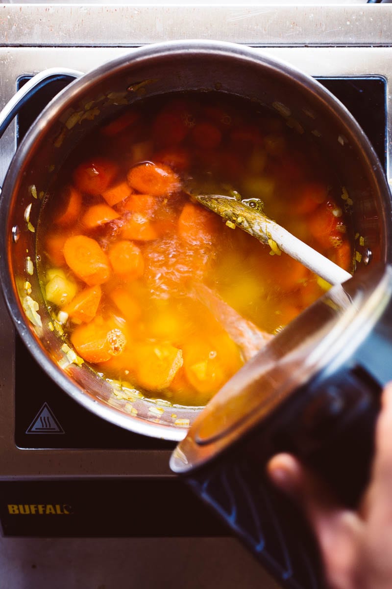 pouring stock into a carrot soup