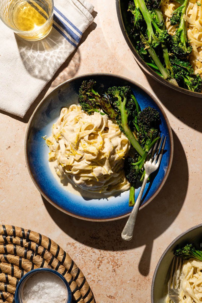 creamy vegan lemon and broccoli pasta in sun on table with other dishes