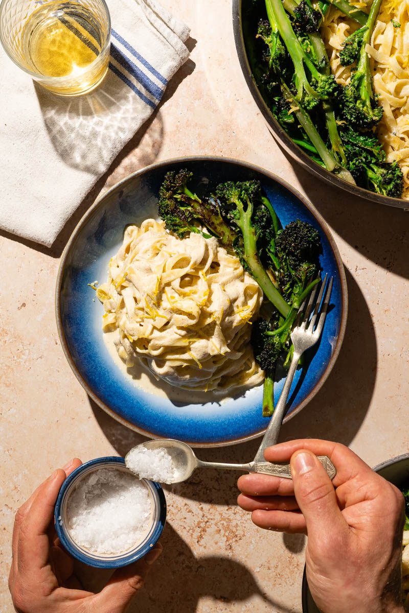 vegan broccoli pasta on table with person serving salt